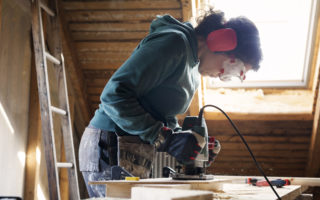 Woman using power tool while renovating old attic